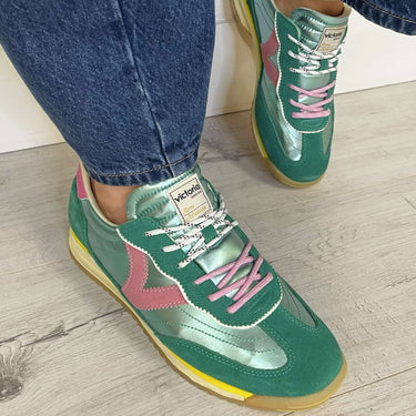 Green sneakers with pink accents worn with blue jeans on a wooden floor.