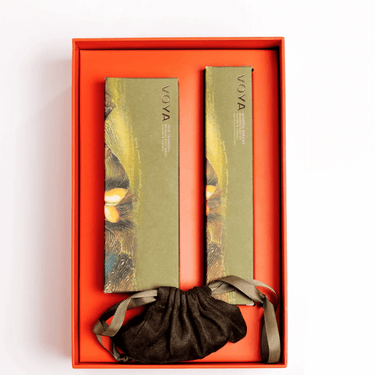 Two green beauty products with a black drawstring bag in an orange box on a white background