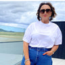 Woman wearing a white top and blue jeans with sunglasses, standing outdoors.