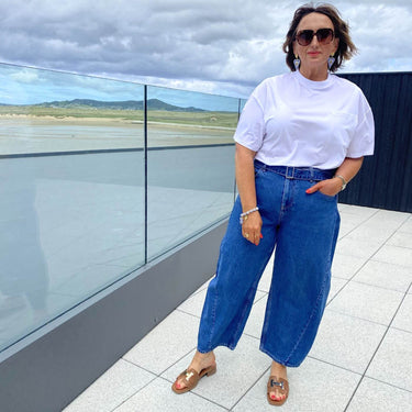 Woman wearing a white t-shirt and blue jeans standing on a rooftop with a scenic view.