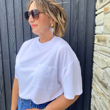 Woman wearing a white t-shirt and sunglasses against a wooden wall.