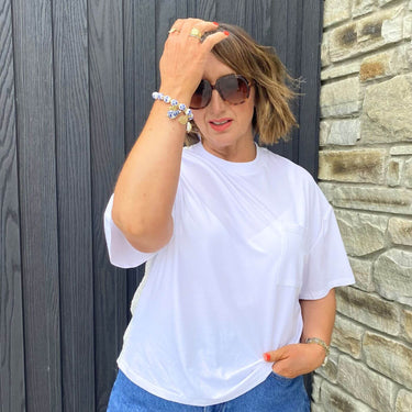 Woman wearing a white t-shirt and sunglasses against a stone wall.