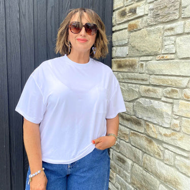 Woman wearing a white t-shirt and blue jeans standing against a stone wall.