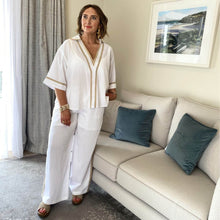 Woman in a white outfit standing in a living room with a beige sofa and blue pillows.