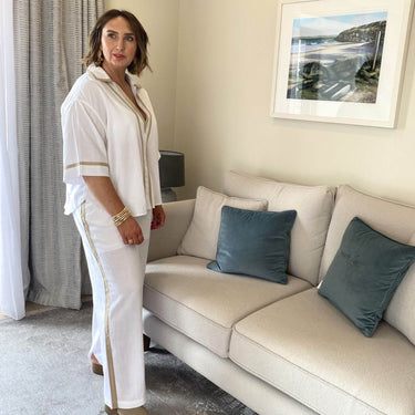 Woman in a white outfit standing next to a beige sofa with blue pillows in a living room.