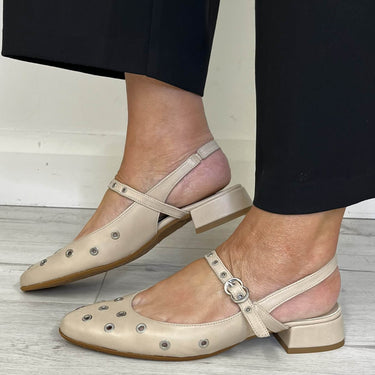 Beige flat shoes worn with black pants on a light wooden floor.
