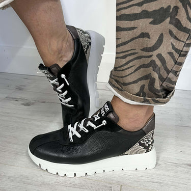 Black and white sneakers worn with patterned pants on a light wooden floor.
