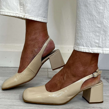 Beige high-heeled shoes worn with light-colored pants on a wooden floor.