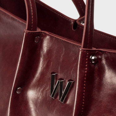 burgundy leather handbag with a metallic logo on a light gray background
