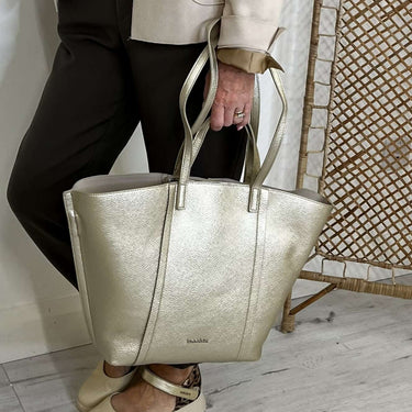 Woman holding a large gold metallic handbag against a white wall