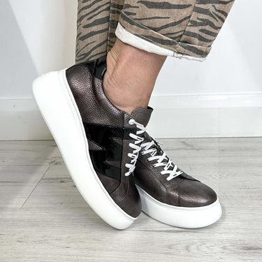 Brown sneakers with white soles worn by a person on a light wooden floor.