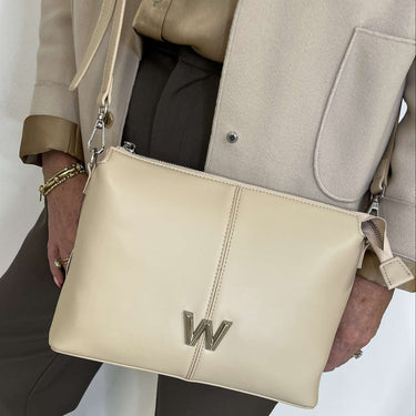Person holding a beige handbag with a letter 'W' emblem on a light background