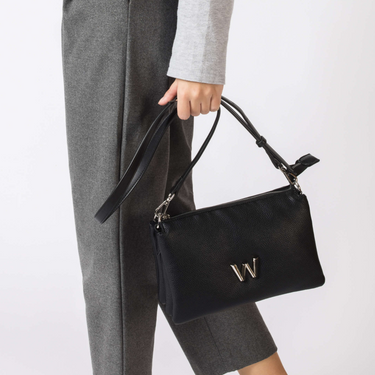 Black handbag with a visible brand logo held by a person wearing gray pants on a white background