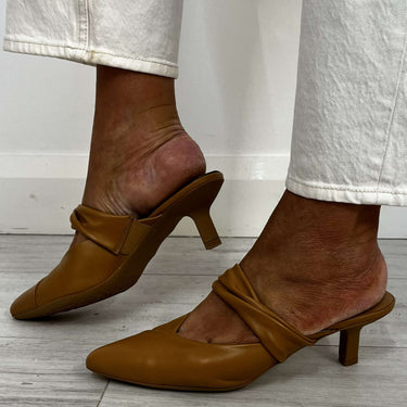 Brown leather shoes worn with light-colored pants on a wooden floor.