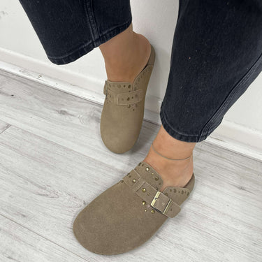 Person wearing brown suede shoes with buckles on a light wooden floor.