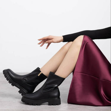 Person wearing black boots sitting on a gray surface with a white background