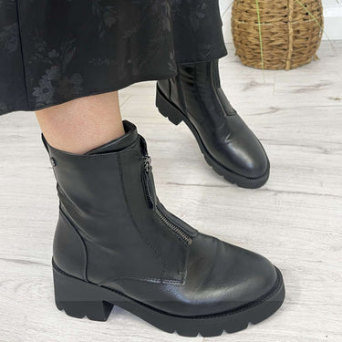 Person wearing black ankle boots with a plant in the background