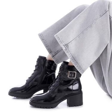 Person wearing black boots and light gray pants on a white background