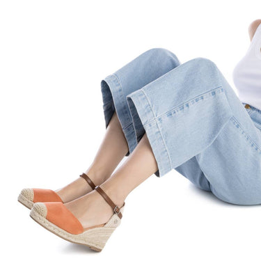 Person wearing orange wedge sandals with a white background
