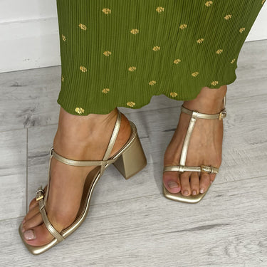 Green patterned pants with gold sandals on a light wooden floor.