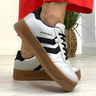 pale silver sneakers with black stripes and brown soles worn with red pants on a light wooden floor.