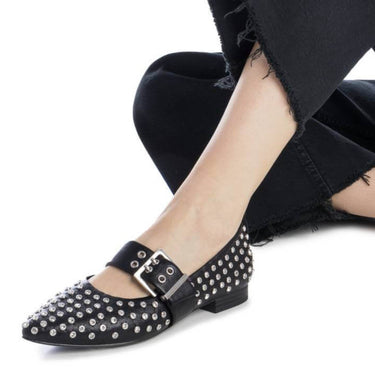 Person wearing black studded flats and black pants on a white background