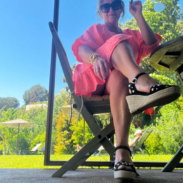 Woman in a pink dress sitting on a chair outdoors with trees and blue sky in the background