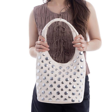 Person holding a white handbag with decorative studs on a white background