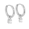 A pair of polished silver huggie hoop earrings, each adorned with a small, clear, square-cut gemstone dangling from the bottom, set against a light gray background with a soft reflection below.